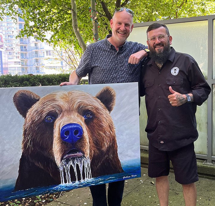 Graham watts and one of his happy art collectors holding graham's painting of a bear with a blue nose outdoors.
