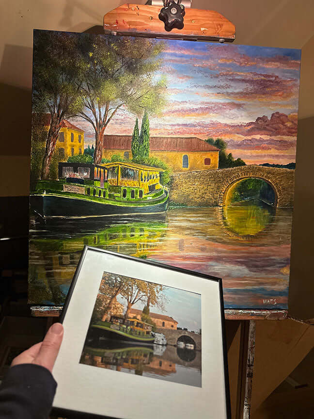 Person presenting a framed waterside landscape artwork by Graham Watts.