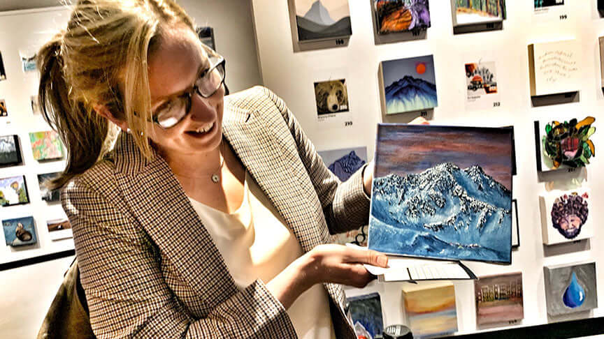 Woman presenting a custom mountain oil painting by Graham Watts in a Vancouver art gallery.