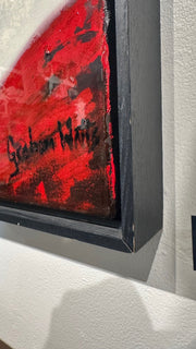 Close-up of a framed abstract artwork with a bold red and black textured design, mounted on a white wall.