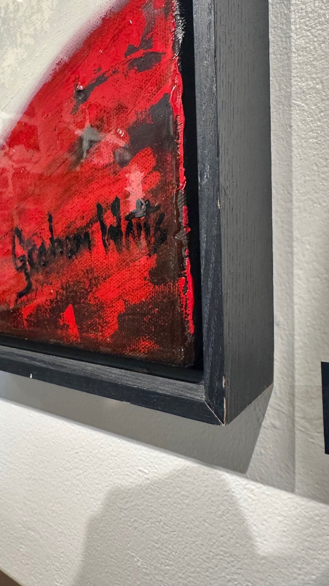 Close-up of a framed abstract artwork with a bold red and black textured design, mounted on a white wall.