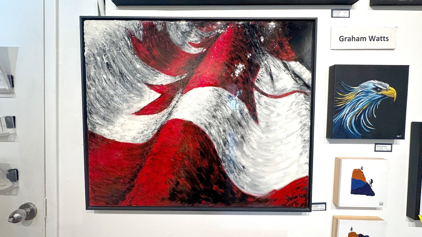 A large framed abstract painting featuring bold red, white, and black brushstrokes, displayed on a white gallery wall alongside other art pieces and a name sign reading Graham Watts.